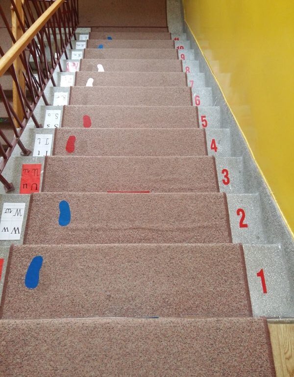 brązowa wykładzina na schodach, przyklejone odciski stó i cyfry od 1 do 9
