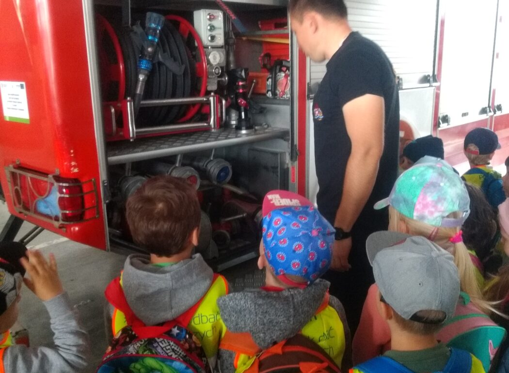 dzieci patrzą na wnętrze samochodu, które im pokazuje strażak