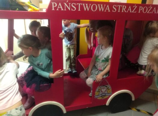 dzieci siedzą w czaerwonym samochodzie z napisem państwowa straż