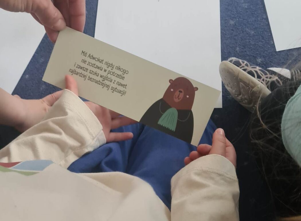 rączki dzieci trzymające kartkę z obrazkiem misia w todze
